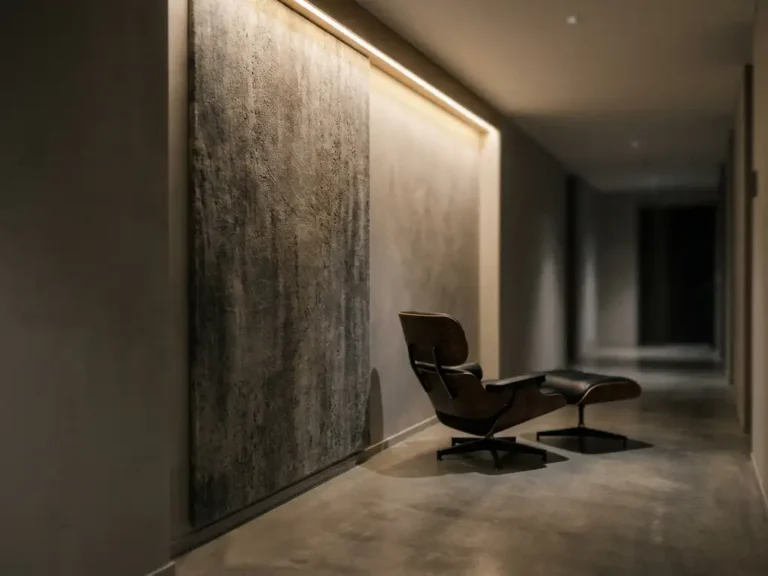 Großformatiges Textilpaneel mit Betonoptik in anthrazit und Warmgrau, installiert in einem minimalistischen Hotelkorridor mit Eames-Stuhl.
